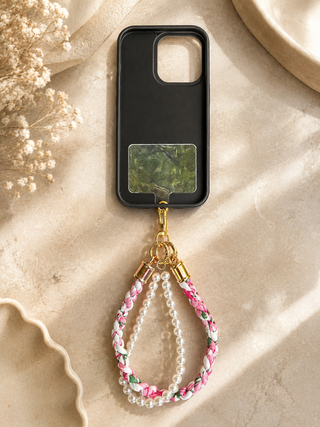 Phone strap with braided floral fabric and white pearl beads attached to a black phone case