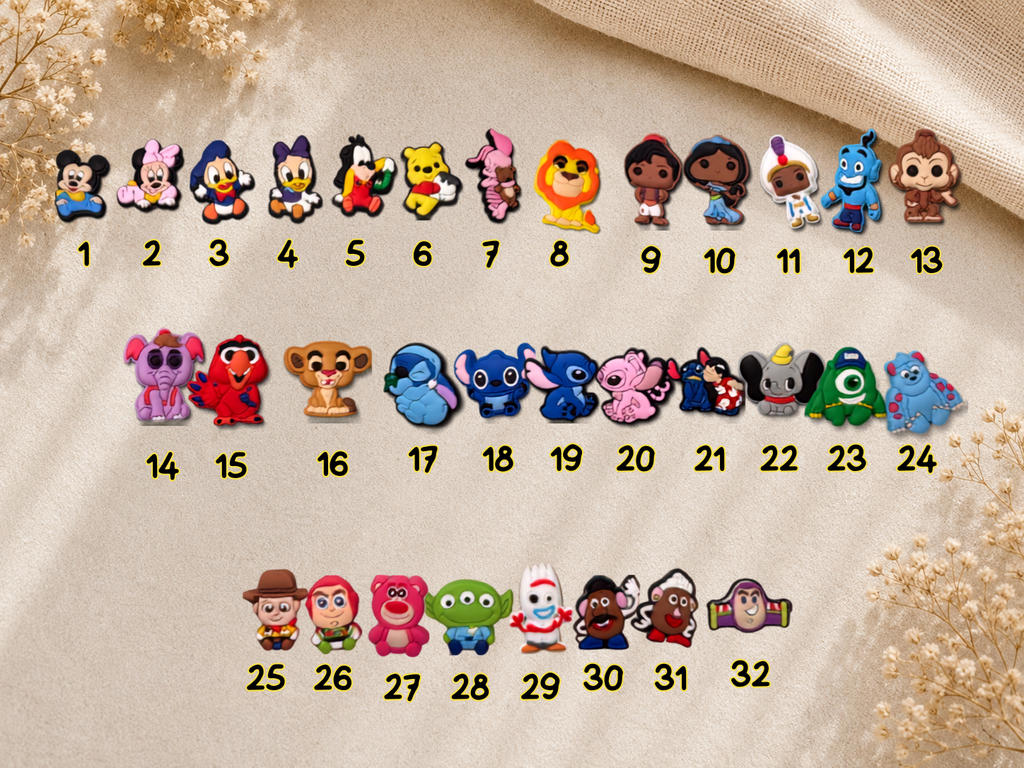 A set of 32 small cartoon character charms or patches arranged in three rows on a beige fabric background with dried flowers. Each charm is numbered 1 through 32 below it.